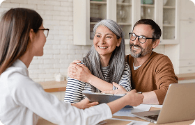 Middle-aged couple smiling while meeting with a debt settlement advisor at a kitchen table