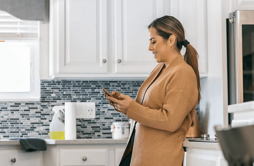 Woman smiling while checking her Momentum debt settlement progress on her phone in her kitchen