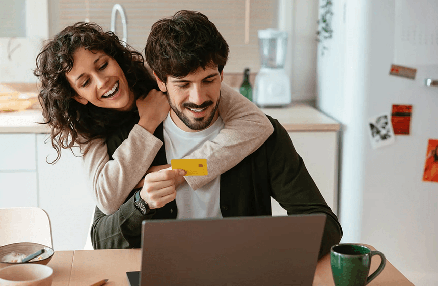 Happy couple at home reviewing finances on a laptop with a credit card, feeling relieved about their debt plan