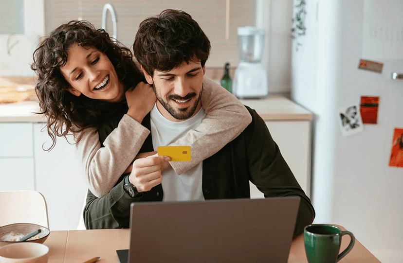 Happy couple at home reviewing finances on a laptop with a credit card, feeling relieved about their debt plan