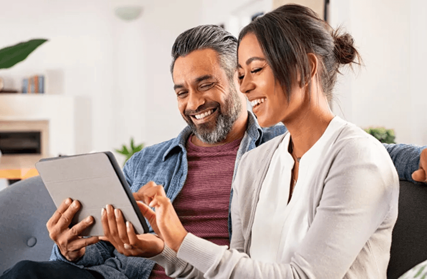 Couple smiling and reviewing their debt settlement plan together on a tablet at home